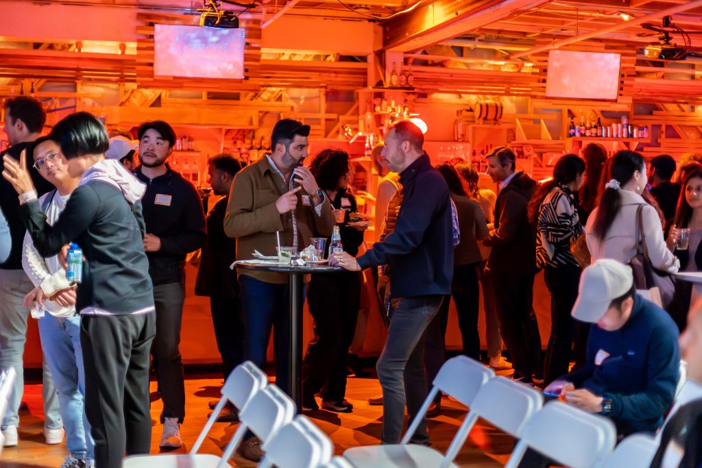 People standing and talking around a table and in front of the Main Room bar.