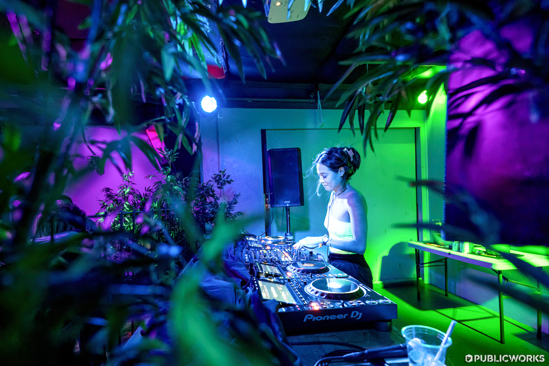 DJ performs in the Loft, photo is shot from behind a plant.